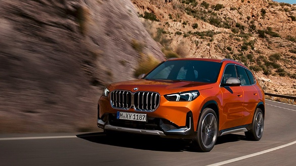 Orangefarbener BMW X1 fährt auf einer Straße durch bergige Landschaft.
