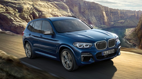 Blauer BMW SUV fährt auf einer kurvigen Straße in einer bergigen Landschaft.