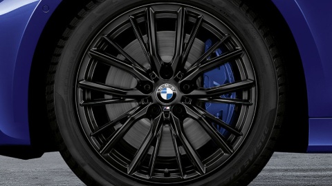 Schwarzes BMW-Leichtmetallrad mit Logo auf grauem Hintergrund, Teil eines blauen Autos.