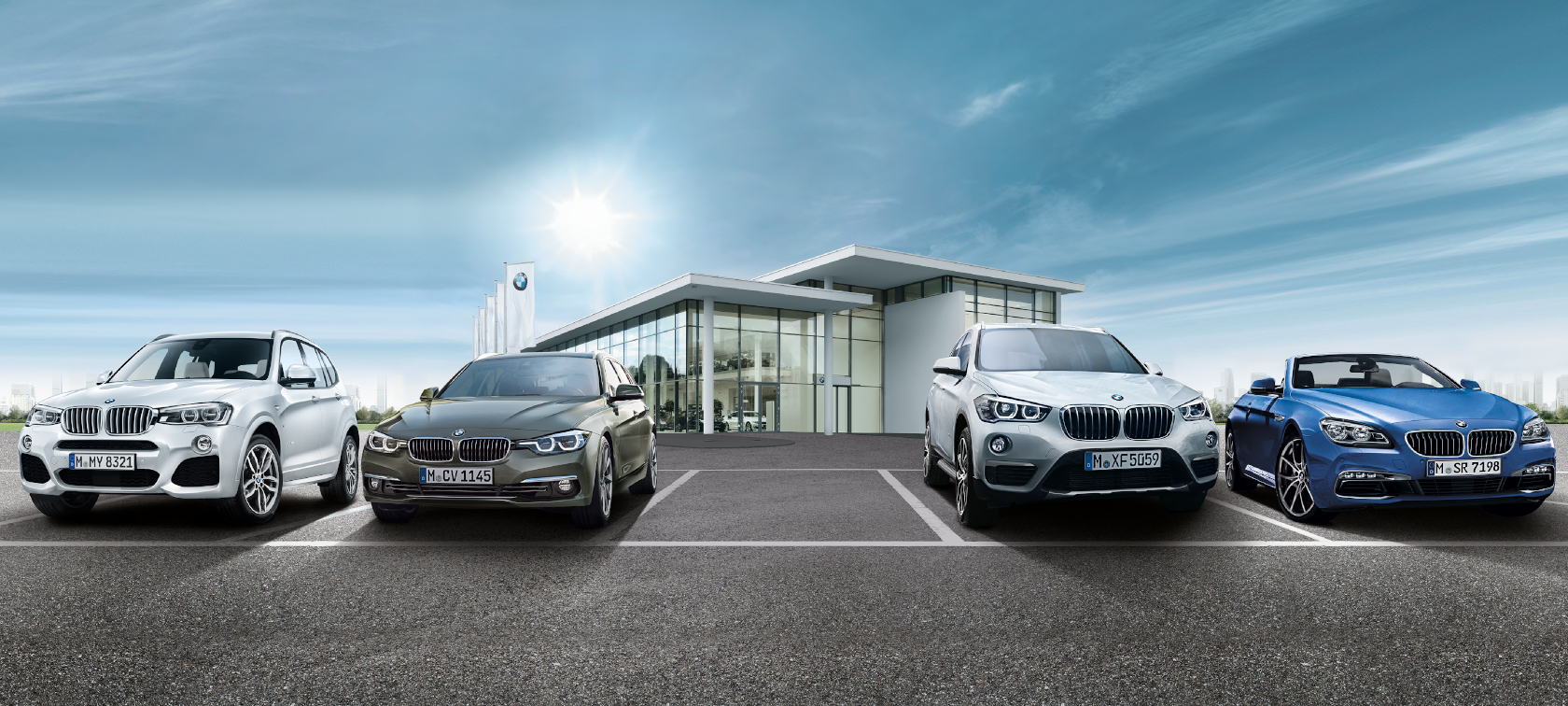 Vier BMW-Fahrzeuge vor einem modernen Autohaus mit Glasfassade und blauem Himmel.