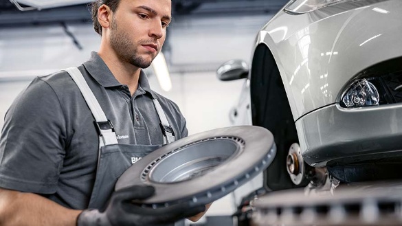 Ein Mechaniker wechselt die Bremsscheibe an einem silbernen Auto in einer Werkstatt.