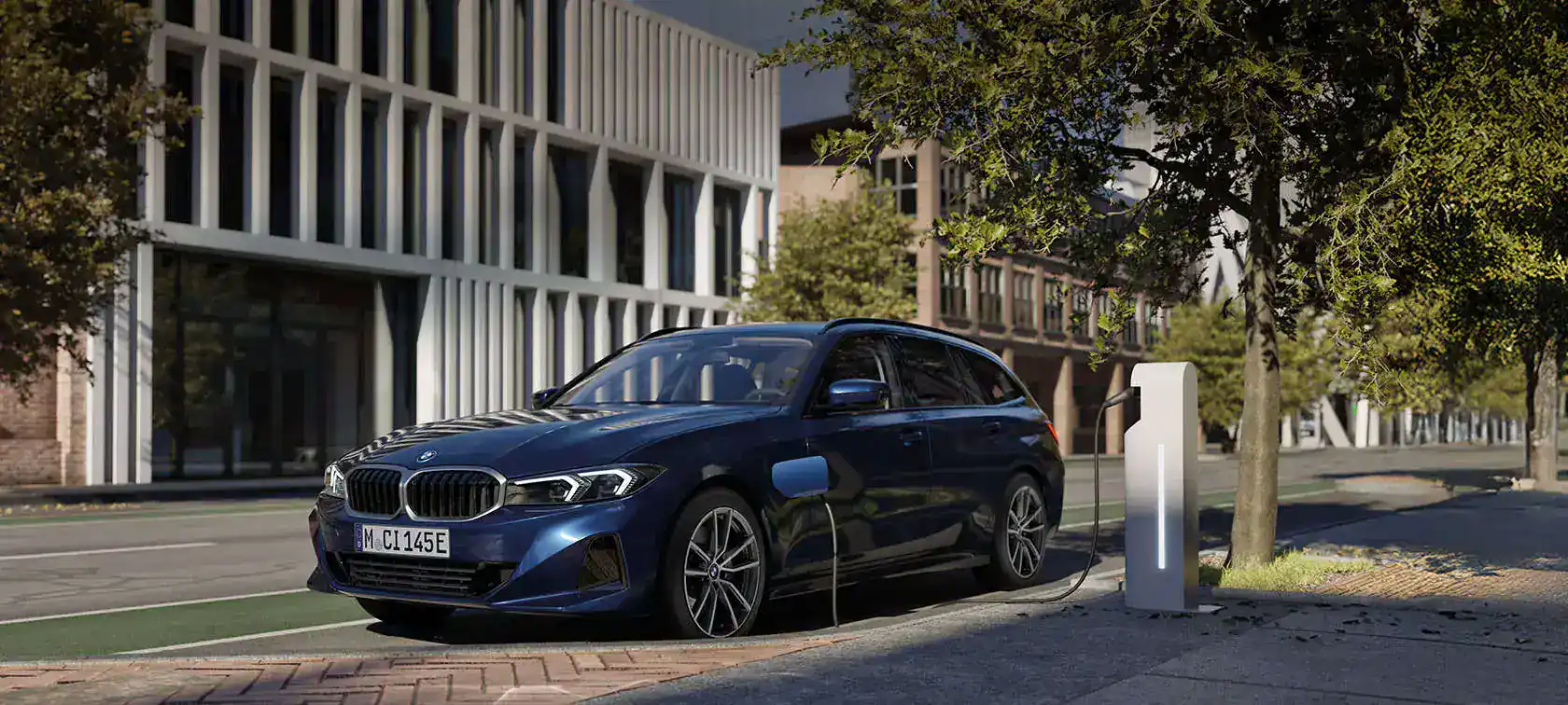 Blauer BMW Kombi an einer Ladestation auf einer städtischen Straße, moderne Gebäude im Hintergrund.