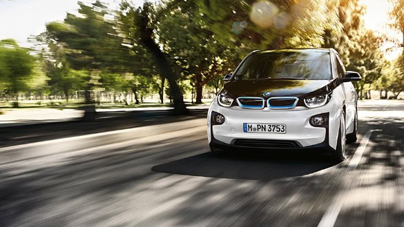 Ein weißer BMW i3 fährt auf einer von Bäumen gesäumten Straße bei Tageslicht.