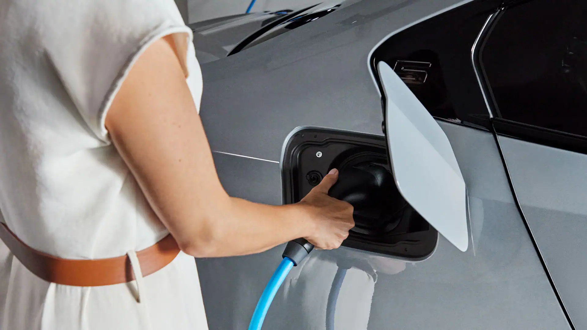 Person lädt ein graues Auto mit einem blauen Ladekabel auf.