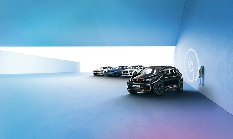 Fünf BMW-Autos in einer blauen Garage, vorne ein schwarzer BMW i3, rechts eine Ladestation.